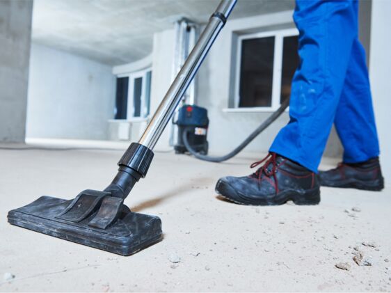 Bauendreinigung in Bremen Mann saugt mit Industriestaubsauger einen dreckigen Boden im Rohbau